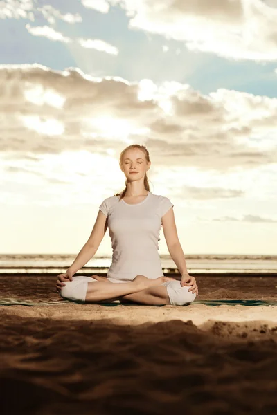 Jonge mooie slanke vrouw praktijken yoga op het strand bij zonsondergang — Stockfoto