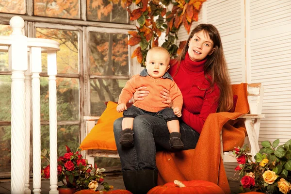 Belle femme avec un enfant sur le porche avant avec des citrouilles au — Photo