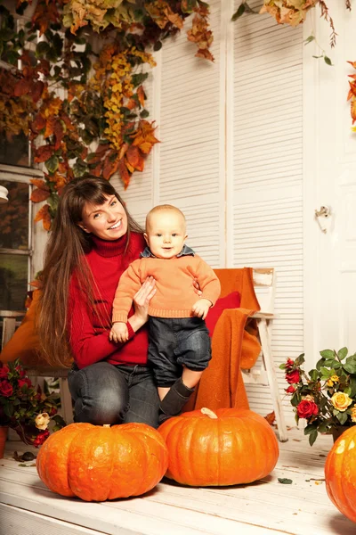 Hermosa mujer con un niño en el porche delantero con calabazas au — Foto de Stock