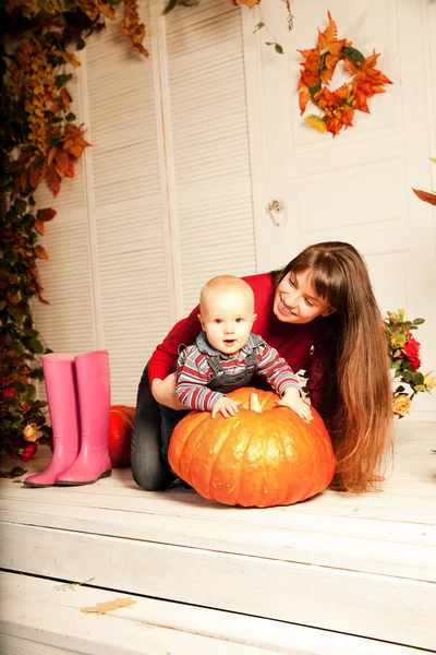 Belle femme avec un enfant sur le porche avant avec des citrouilles au — Photo