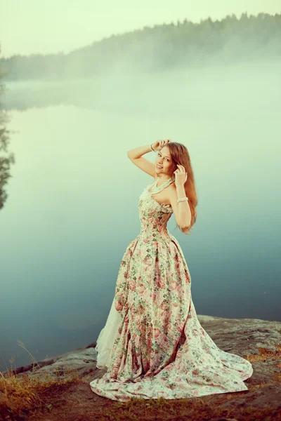 Mulher de luxo em uma floresta em um vestido vintage longo perto do lago . — Fotografia de Stock