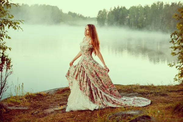 Mulher de luxo em uma floresta em um vestido vintage longo perto do lago . — Fotografia de Stock