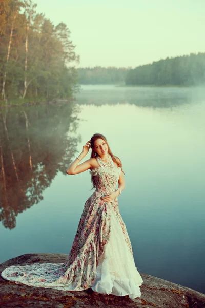 Lyx kvinna i en skog i en lång vintage klänning nära sjön. — Stockfoto