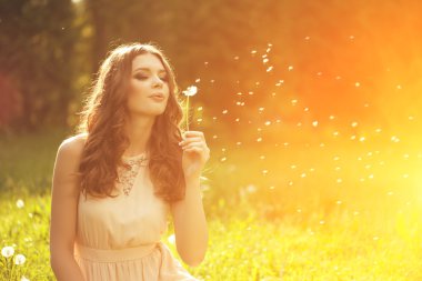 Beautiful young woman blowing a dandelion. Trendy young girl at 