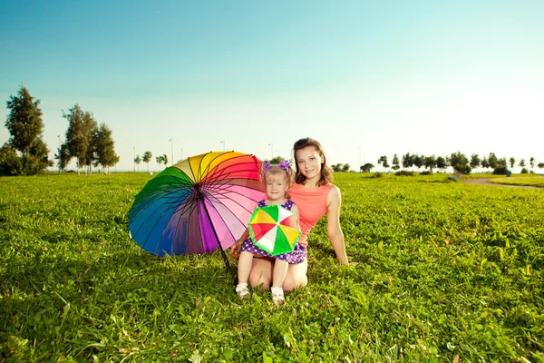 Niedliches kleines Mädchen mit Mutter Regenbogen Regenschirm hält in der p — Stockfoto