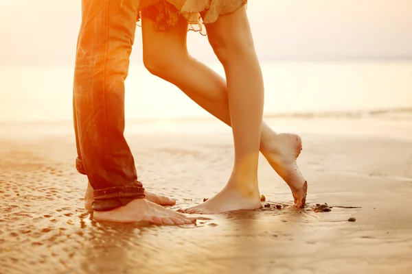 Um jovem casal amoroso abraçando e beijando na praia ao pôr do sol — Fotografia de Stock