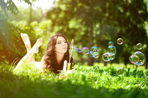 Woman and soap bubbles in park. Beautiful young girl lying on th