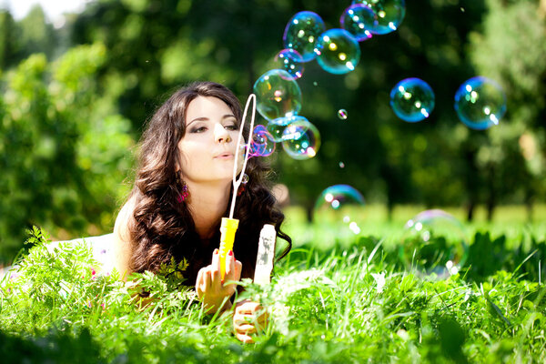 Woman and soap bubbles in park. Beautiful young girl lying on th