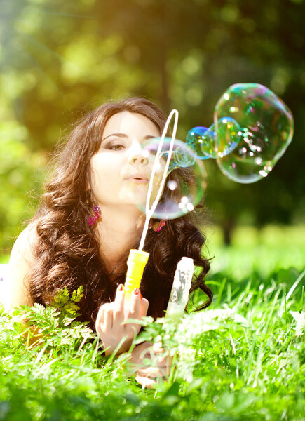 Woman and soap bubbles in park. Beautiful young girl lying on th