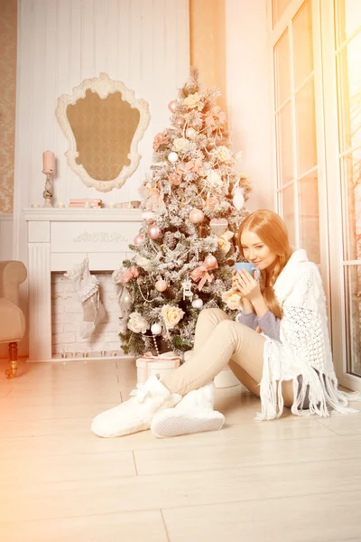 Beautiful young woman drinking tea at the Christmas tree. Beauti — Stock Photo, Image