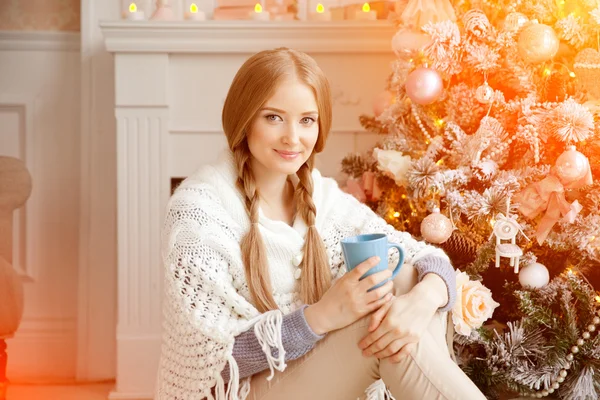 Schöne junge Frau trinkt Tee am Weihnachtsbaum. Schön — Stockfoto