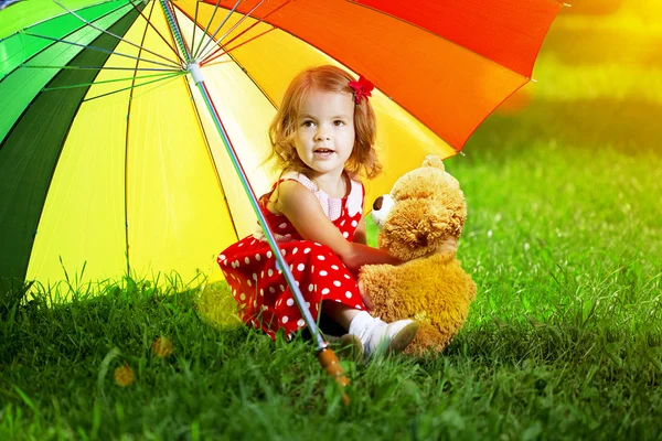 Menina feliz com um guarda-chuva arco-íris no parque. Brincar com crianças Imagem De Stock