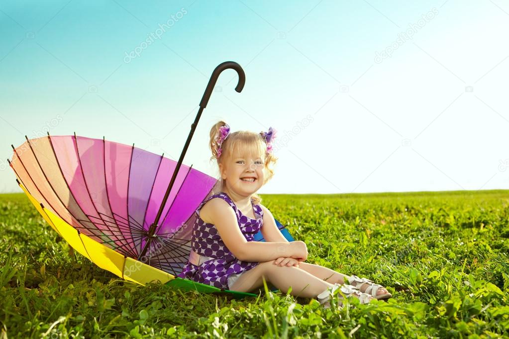 Beautiful little girl with rainbow umbrella on the grass in the 