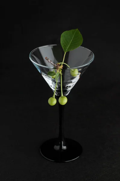 Unripe green cherry in martini glass on black — Stock Photo, Image