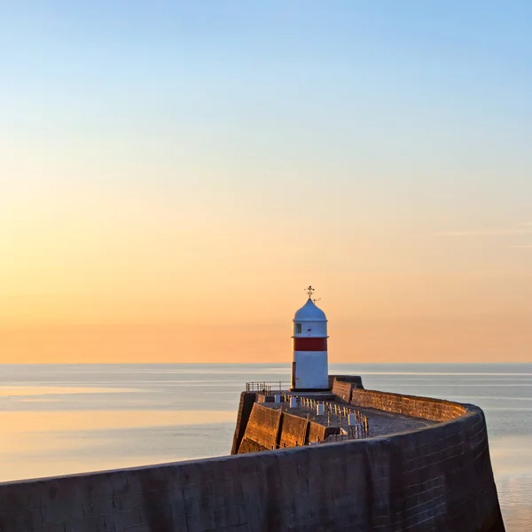 平静的海上日出时防波堤墙上的灯塔 — 图库照片