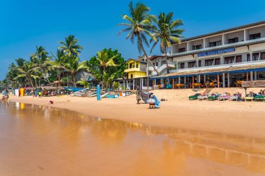HIKKADUWA, SRI LANKA - 22 Ocak 2014: Hikkaduwa 'daki Narigama Sahili' nde güneşli yataklarda ve arka planda küçük restoranlarda insanlar