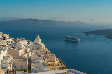FIRA, GREECE - MAY 21.2022: View to the houses of Fira at sunset, background a cruise ship, sea and Volcano of Santorini island