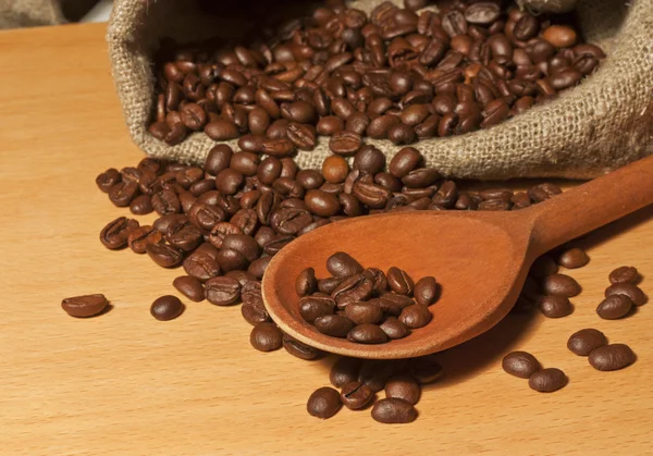 Granos de café en un saco y un fondo de cuchara de madera —  Fotos de Stock