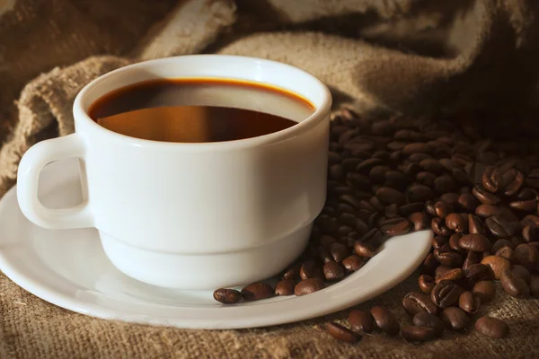 White cup of coffee on sacking and coffee beans — Stock Photo, Image