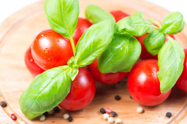 Tomatoes and basil leaves on wooden cutboard — Stock Photo, Image
