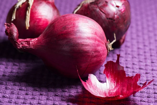 Cipolle rosse su tovaglia viola — Foto Stock