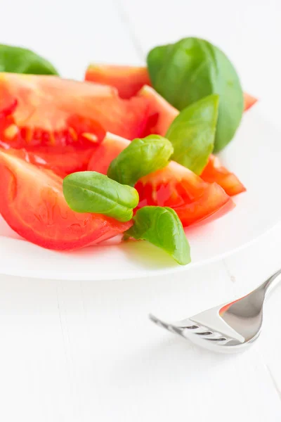 Φρέσκες ντομάτες με βασιλικό φύλλα σε ένα πιάτο — Φωτογραφία Αρχείου