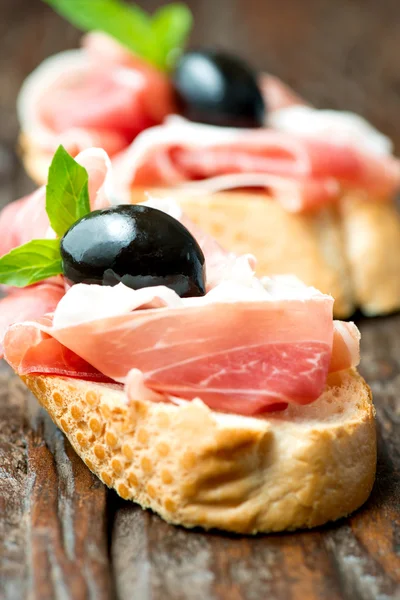 Sanduíches com azeitona prosciutto na tábua de corte de madeira vertica — Fotografia de Stock