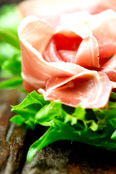 Prosciutto and salad leaves on wooden old table close up — Stock Photo, Image