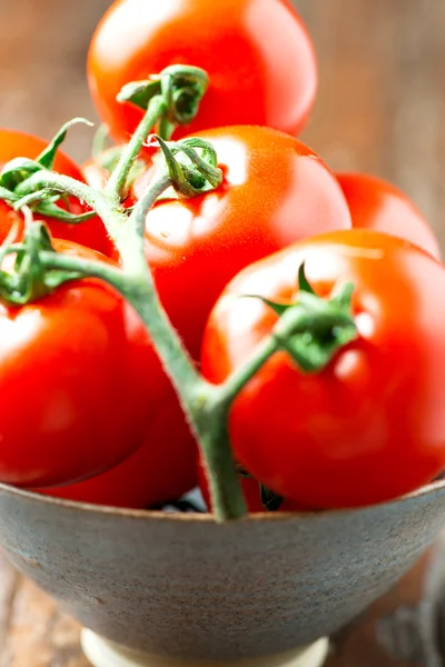 Tomatoes in a bowl on old wooden table vertical macro — Stock Photo, Image