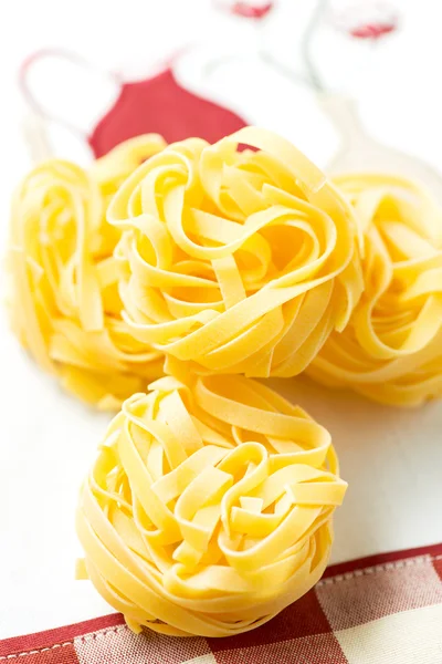 Ninhos de macarrão seco tagliatelle na toalha de mesa vertical e vermelho — Fotografia de Stock