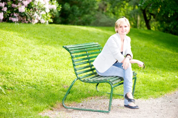 Ung kvinna sitter på en bänk i parken och leende — Stockfoto