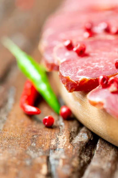 Cured meat with chilli pepper on wooden table — Stock Photo, Image