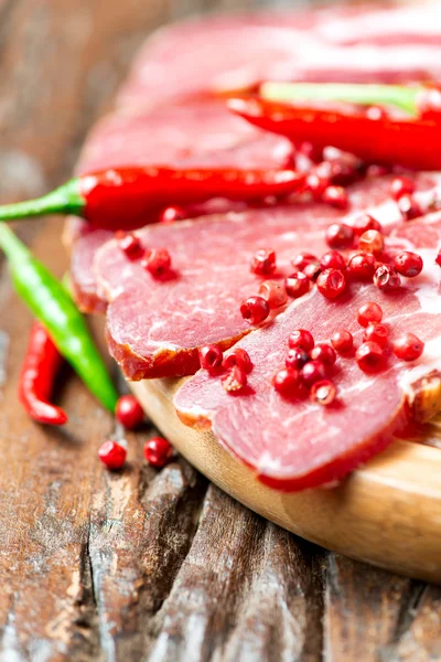 Cured meat with red chilli pepper on wooden table — Stock Photo, Image