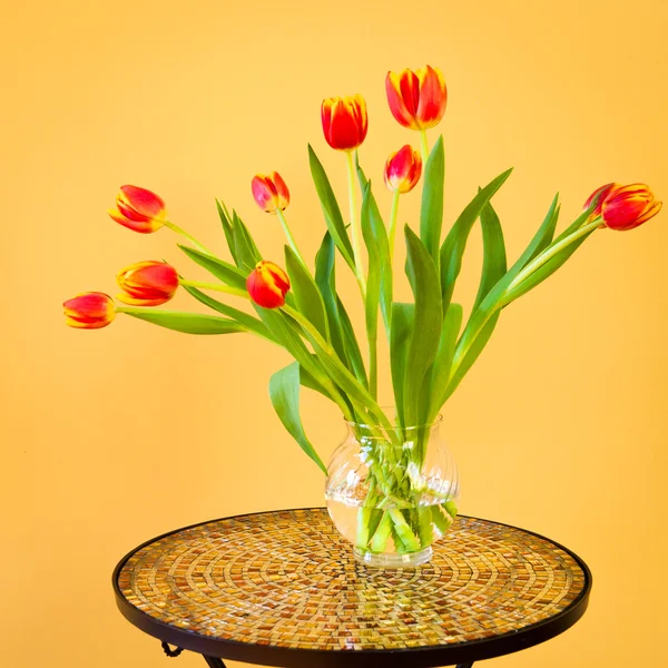 Red tulips in a vase on mosaic table. — Stock Photo, Image