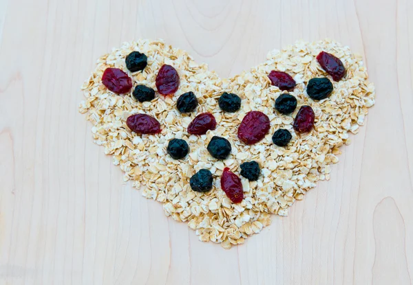 Whole grain oats with dried cranberries and blueberries in heart — Stock Photo, Image