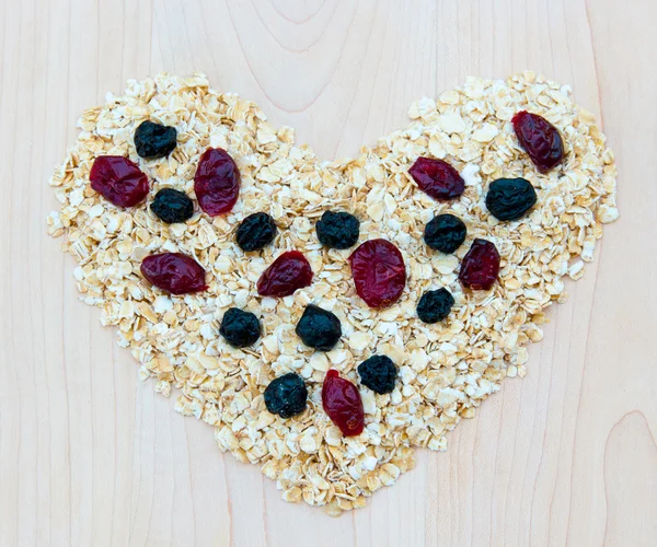 Whole grain oats with dried cranberries and blueberries in heart — Stock Photo, Image