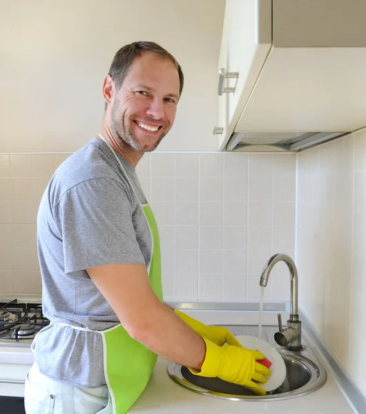 Uomo sorridente che lava i piatti in cucina — Foto Stock