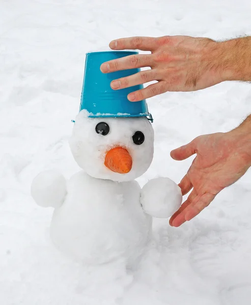 Man's hands sculpt snowman with blue bucket — Stock Photo, Image