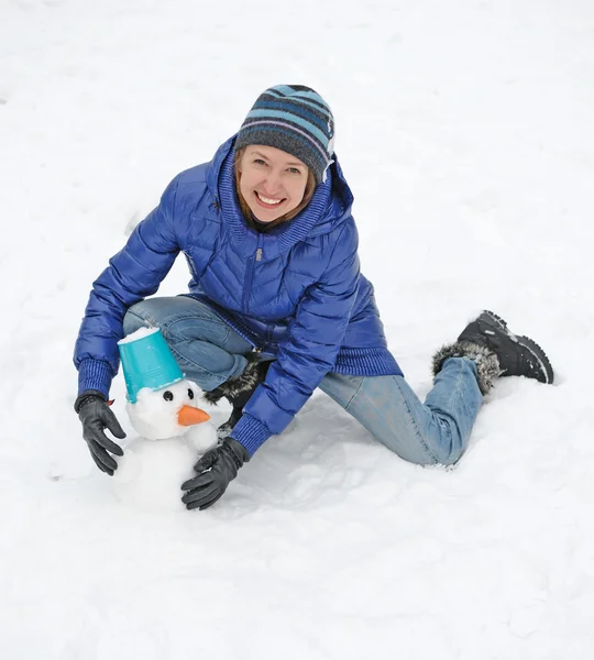 Smiling woman sculpts snowman with blue bucket — Stock Photo, Image