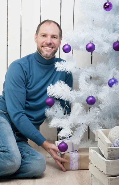 Glimlachende man in het blauw in de buurt van een kerstboom — Stockfoto