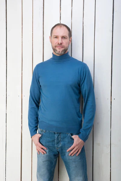 Homme souriant au col de poloneck bleu au mur blanc — Photo