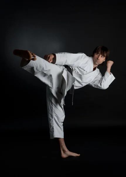 Hombre haciendo karate patada con el pie sobre un fondo negro —  Fotos de Stock