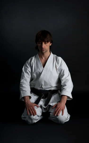 Человек в кимоно с черным поясом медитирует на черной спине — стоковое фото