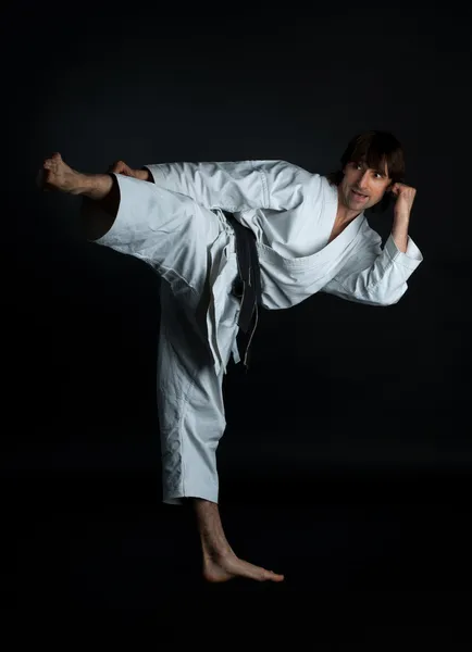 Hombre haciendo karate patada con el pie sobre un fondo negro — Foto de Stock