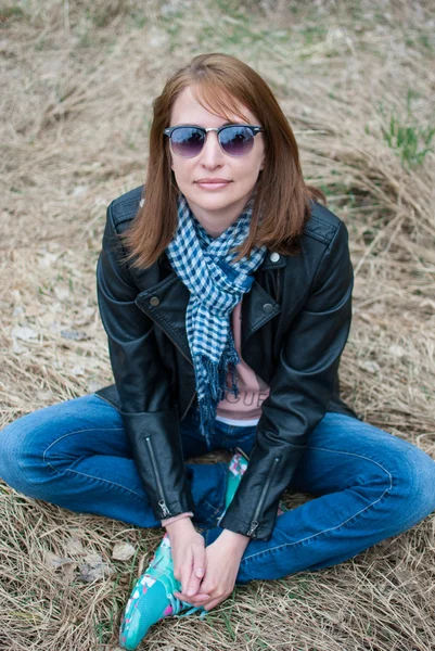 Junge Frau in schwarzer Jacke und Jeans auf dem Heu sitzend — Stockfoto