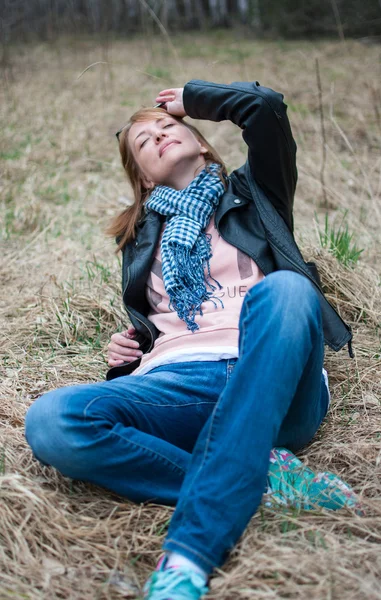 Young woman in a black jacket and jeans sitting on the hay — Stock Photo, Image