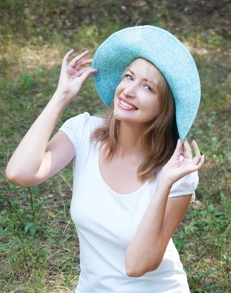 Lovely girl in blue hat on a background of forest green — Stock Photo, Image