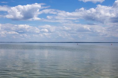 Kar beyazı bulutlar ve yazın sakin, temiz bir göl, temizlik ve sükunet.