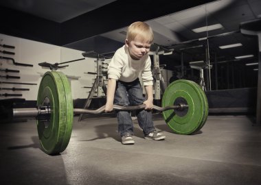 Determined young boy trying to lift a heavy weight bar clipart