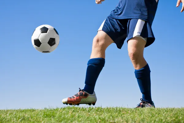 Спортсмен пинает футбольный мяч по полю — стоковое фото